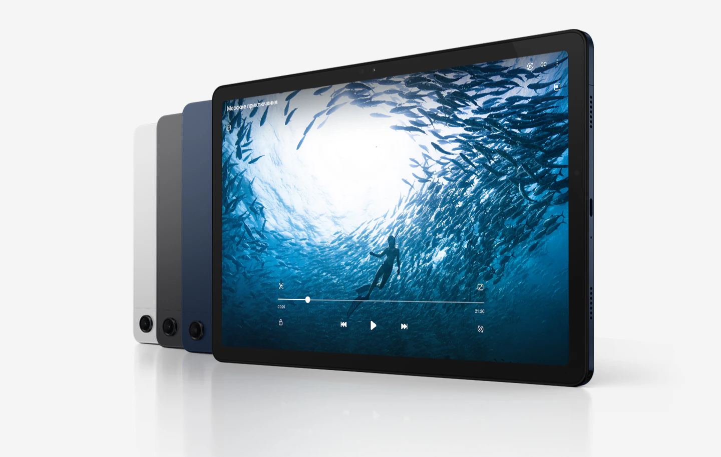 Четыре планшета Galaxy Tab A9+ расположены по диагонали. Три устройства обращены к зрителю задней панелью, а планшет на переднем плане показан со стороны экрана. Цвета устройств слева направо: &laquo;Серебристый&raquo; и &laquo;Графитовый&raquo;, а остальные &mdash; &laquo;Темно-синие&raquo;. На экране устройства справа окно с видео под названием Морские приключения, в котором виден человек, плывущих в океане в окружении рыб.