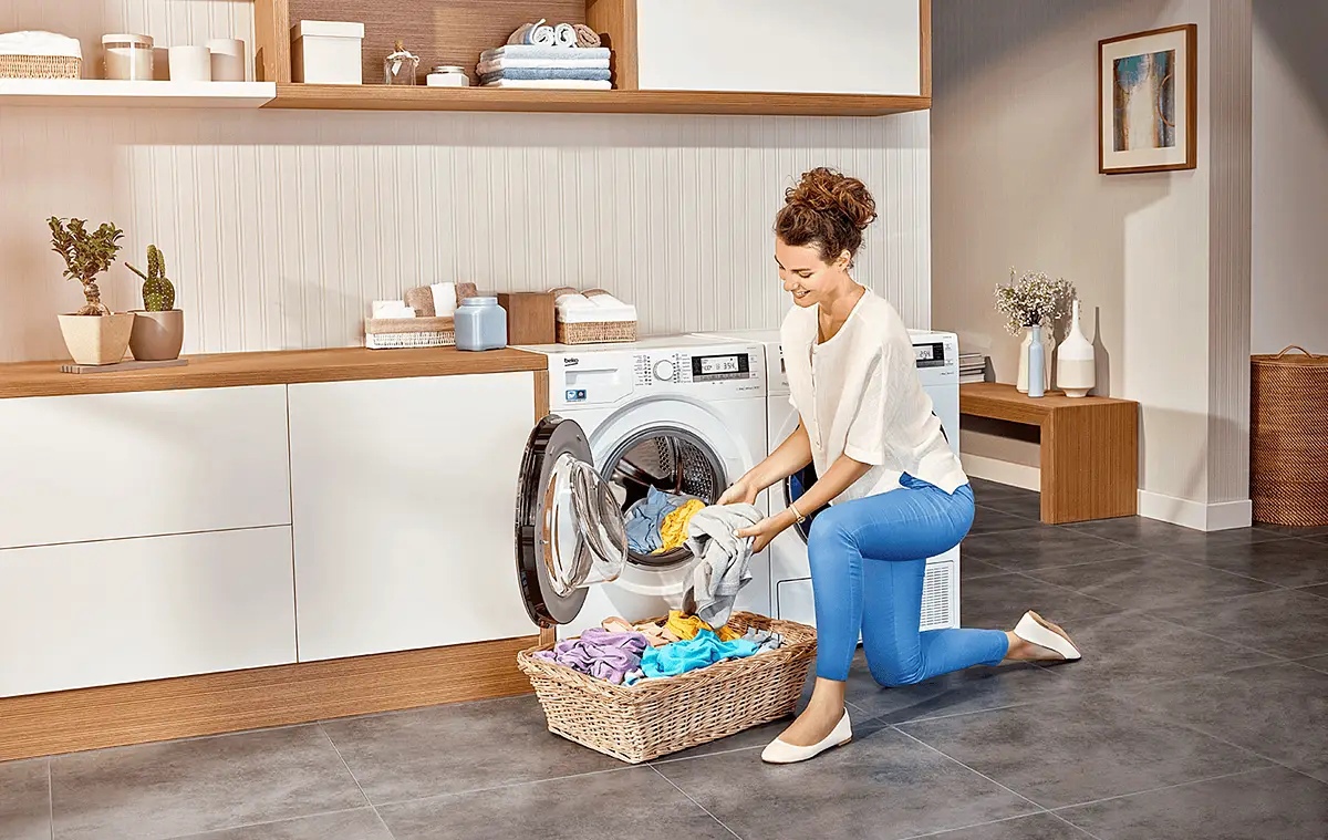 Beko WSRE6H612ZAWI фронтальная загрузка — женщина загружает бельё в барабан